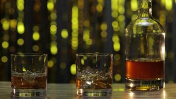 Barman pushes, puts two glasses with golden whiskey, cognac or brandy with ice cubes on wooden table video
