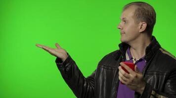 Rocker man showing side advertising area. Using smartphone, pointing at wall for your text, logo video
