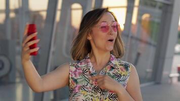 Tourist girl wearing trendy sunglasses uses phone. Using smartphone for call, talk. Trip, tourism video
