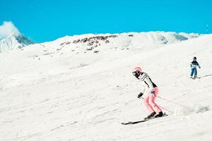 Woman mother skier with child son boy on the piste ski downhill fast motion in Alps. Active winter holidays, skiing downhill in sunny blue sky day. Ski rides on the track with swirls of fresh snow photo
