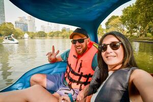 Happy young caucasian couple take selfie look at camera enjoy sport activity on pedal boat in famous public Lumphini park in summer. Bangkok relaxation leisure activities photo