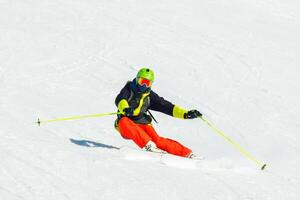 Front view male skier wear colorful outfit isolated on piste ski downhill fast motion in Alps. Active winter holidays, skiing downhill in overcast day. Ski rides on the track with swirls of fresh snow photo