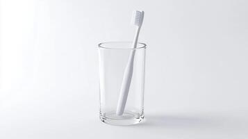 A simple white toothbrush stands upright in a clear glass tumbler on a smooth, light background photo