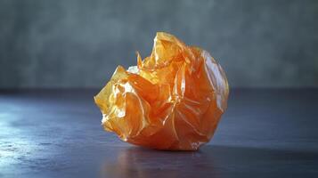 Crumpled orange plastic wrapper on a textured surface indoors in soft lighting photo