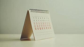 A small, spiral-bound desk calendar displaying the days of the month on a minimalist surface in a bright, natural light setting photo
