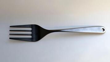 A metallic three-pronged fork lying flat against a white background photo