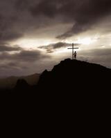 Silhouette of hopeful woman standing alone by cross search for purpose on scenic hilltop viewpoint with dramatic sky background sunshine on sunset.Conceptual loneliness, despair, search for purpose photo