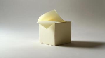A plain cream-colored cube with a slightly curled yellow note sticking out on a neutral background in soft light photo