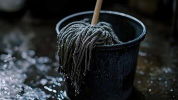 Wet mop resting in a bucket on a shiny floor in a cleaning area during daylight photo