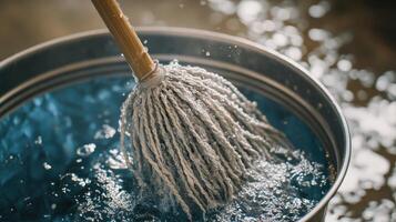 A mop soaking in blue water inside a metal bucket on a reflective surface photo