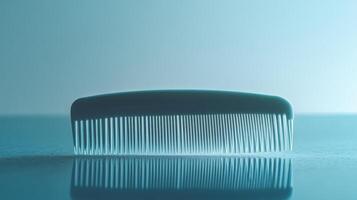 A plastic comb resting on a reflective surface with soft blue lighting in a minimalist setting photo