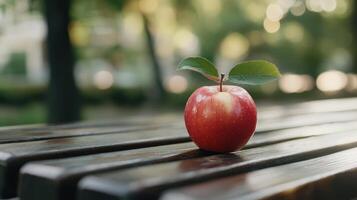 Fresh Red Apple With Green Leaves Sitting on Wooden Table in a Sunny Park During the Afternoon photo
