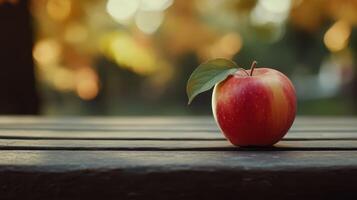 Fresh Red Apple Resting on Wooden Table Amidst Autumn Foliage in Golden Hour Light photo