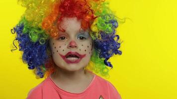 Little child girl clown in colorful wig tells something interesting. Having fun, smiling. Halloween video