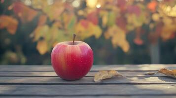Fresh Red Apple Resting on Wooden Table Surrounded by Colorful Fall Leaves in Late Afternoon Light photo