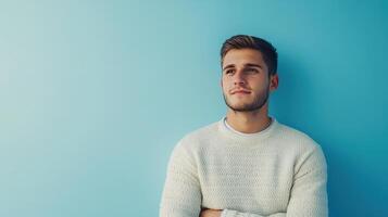 Young man in a light sweater thoughtfully gazing at a blue wall in a relaxed indoor setting during the daytime photo