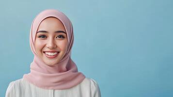 Smiling young woman wearing a pink hijab against a blue background, captured during daylight in an indoor setting photo