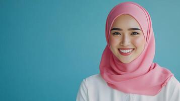 Smiling young woman in pink hijab against a blue background during daylight photo