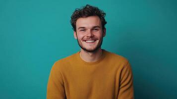 Smiling young man with curly hair wearing a yellow sweater against a teal background photo