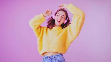 Young woman enjoying music while dancing in a cozy yellow sweater against a pink background photo