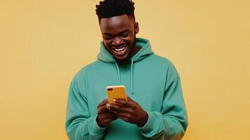 Young man in a green hoodie smiles while using a smartphone against a bright yellow background photo