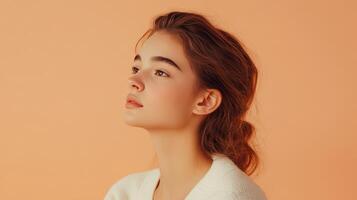 Young woman with flowing hair poses gracefully against a soft peach background during a serene indoor photoshoot photo