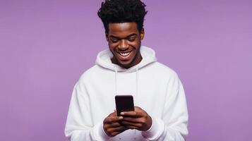 Young man smiling while using a smartphone against a purple background in a casual setting photo