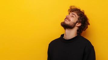 Young man smiling against vibrant yellow background in casual black attire during a joyful moment photo