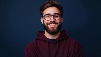 Young man with beard and glasses smiling warmly against a dark blue background photo