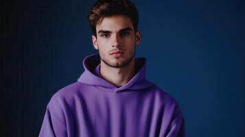 Young man in a purple hoodie stands against a dark blue background, looking thoughtfully into the camera photo