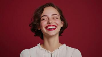 A woman with curly hair smiles joyfully against a deep red background, showcasing her bright red lipstick and stylish attire photo