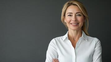 Confident woman in a white blouse standing against a dark background, smiling warmly during daylight photo