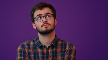 Young man in checkered shirt thinking against a purple wall backdrop in a relaxed indoor setting photo