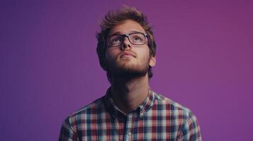 Young man in plaid shirt looking up against a vibrant purple background, capturing a moment of contemplation in an indoor setting photo