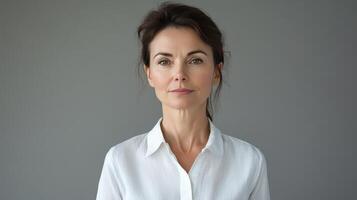 A woman in a white shirt poses against a gray backdrop in a calm and composed manner during a studio session photo