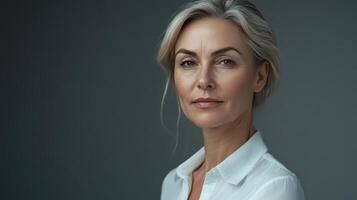 A confident woman in a white shirt poses against a neutral background during the day, showcasing a thoughtful expression photo