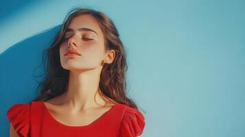 Young woman in a red top relaxing against a blue wall on a sunny day, with soft light accentuating her features photo