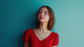 Young woman in a red dress posing against a teal backdrop in a well-lit indoor setting photo