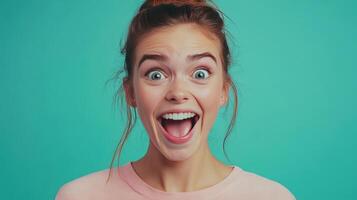 Young woman smiling widely against a bright turquoise background with a playful expression, capturing joy and enthusiasm during a casual moment photo