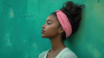 Young woman posing against a vibrant green wall while wearing a pink headband, showcasing her profile in soft light photo