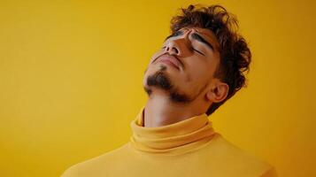 A young man in a yellow turtleneck sweater poses against a vibrant yellow background, showcasing a mood of contemplation photo