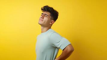 Man experiencing back pain while standing against a bright yellow background in a casual setting photo