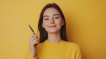 Woman smiling while holding a pen against a bright yellow background in a casual setting photo