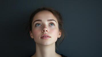 Young woman gazing upwards, with soft lighting and a neutral gray background, capturing a moment of contemplation and serenity indoors photo