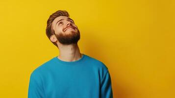 Young man with a beard smiling and looking up against a bright yellow background indoors photo