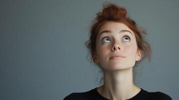 Woman with red hair looking upwards against a gray background during a thoughtful moment photo