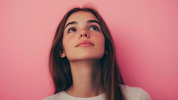 Young woman gazing upward against a pink wall, expressing curiosity and contemplation in a creative indoor setting photo