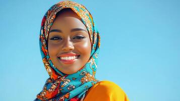 Smiling woman wearing a colorful headscarf against a clear blue sky in a sunny outdoor setting photo