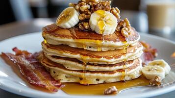 Delicious stack of pancakes topped with bananas, walnuts, and syrup served with crispy bacon photo