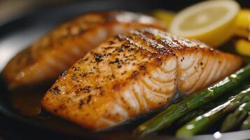 Grilled salmon fillets served with asparagus and lemon wedges on a dark plate photo